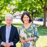 Two smiling women in the countryside in front of trees.
