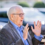 Older man in gray jacket gesticulates